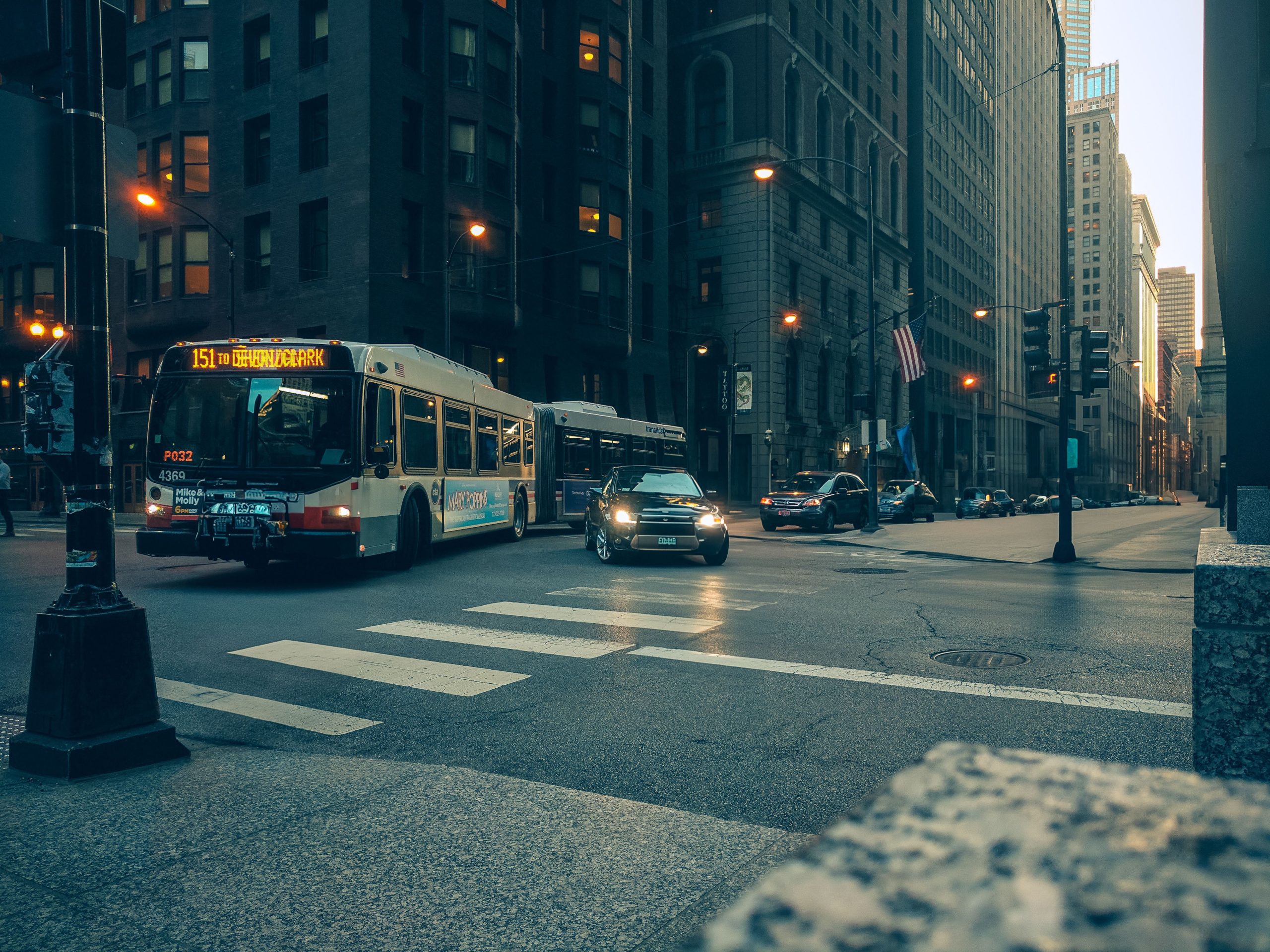 City bus and cars navigate a downtown intersection at twilight, urban USA setting.