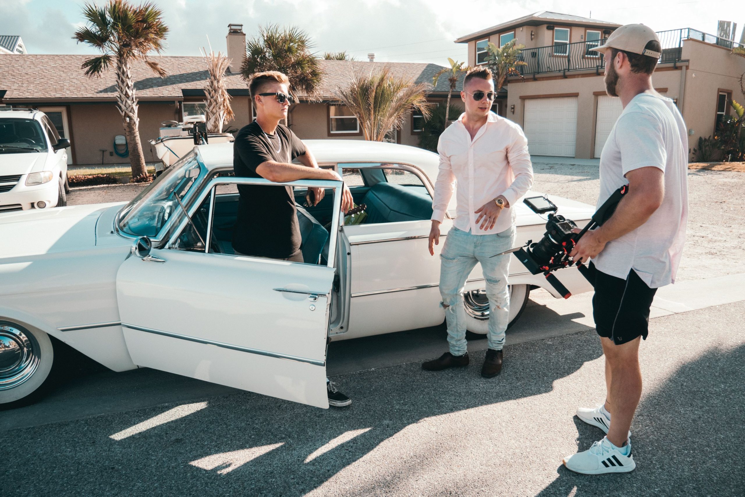 Production Crew Transportation in NYC: 7 Smart Ways to Move Your Crew Effortlessly in 2026 3 Three men with camera equipment near a classic car on a sunny day, showcasing filming outdoors.