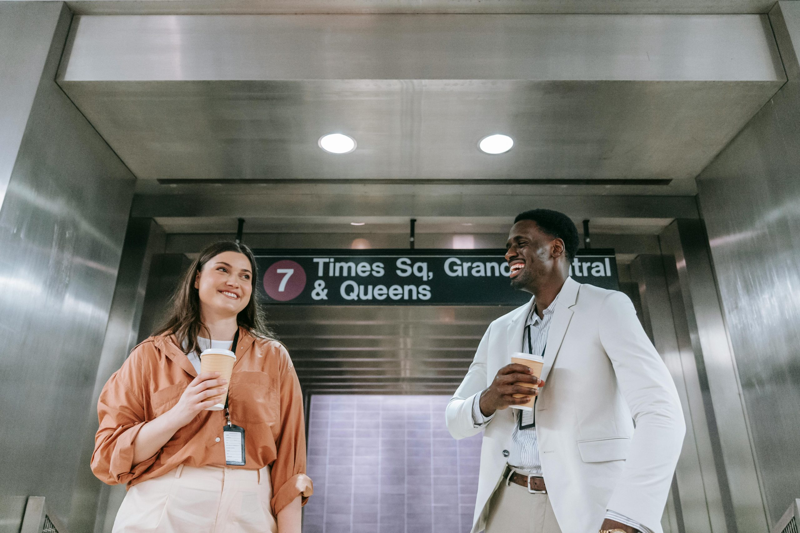 Employee Shuttle Service NYC: 7 Honest Seasonal Booking Facts for 2026 2 Two colleagues laugh and hold coffee near a subway sign in an underground station.