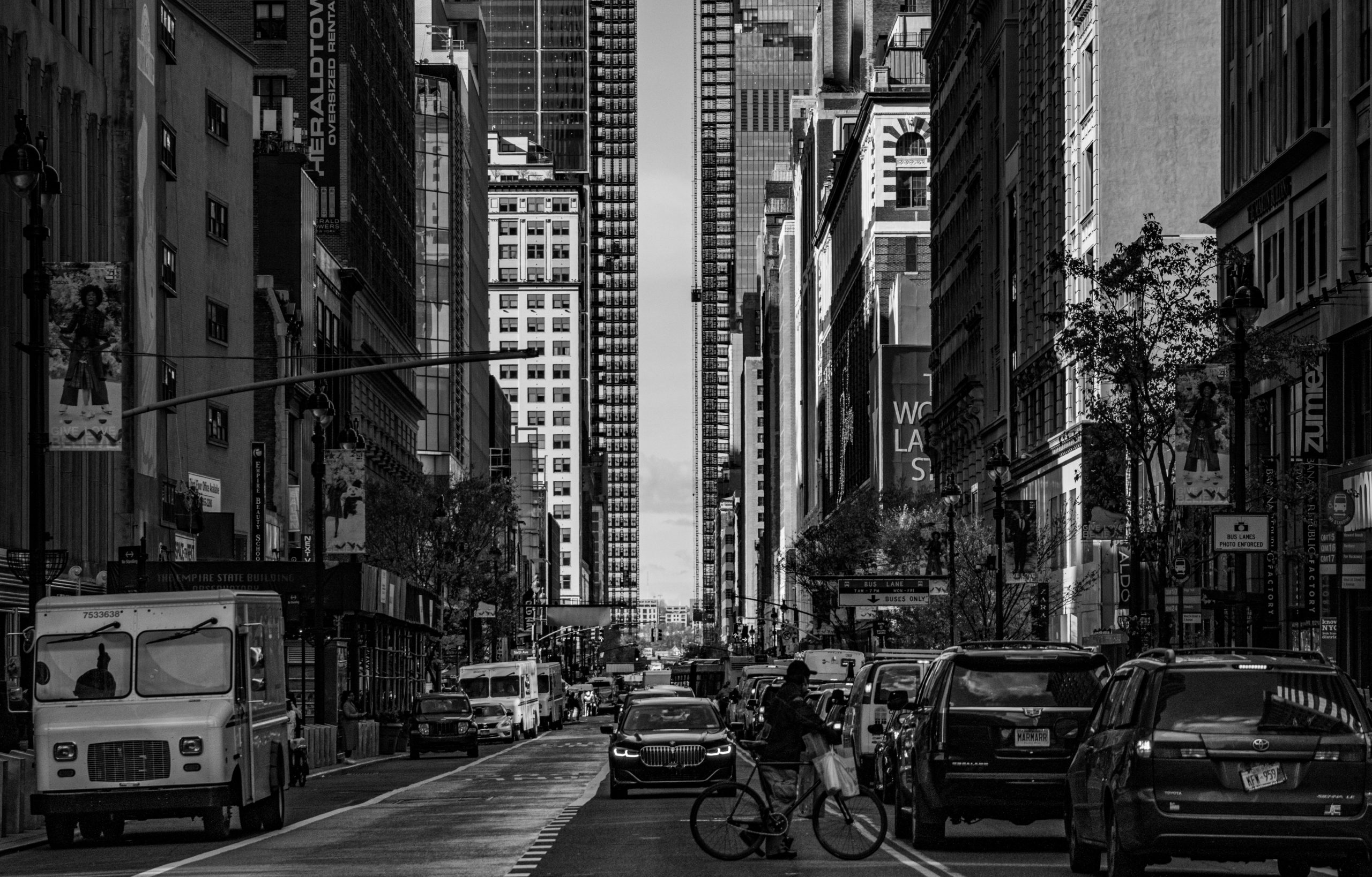 Black and white photo capturing bustling street scene with cars and buildings in New York City.