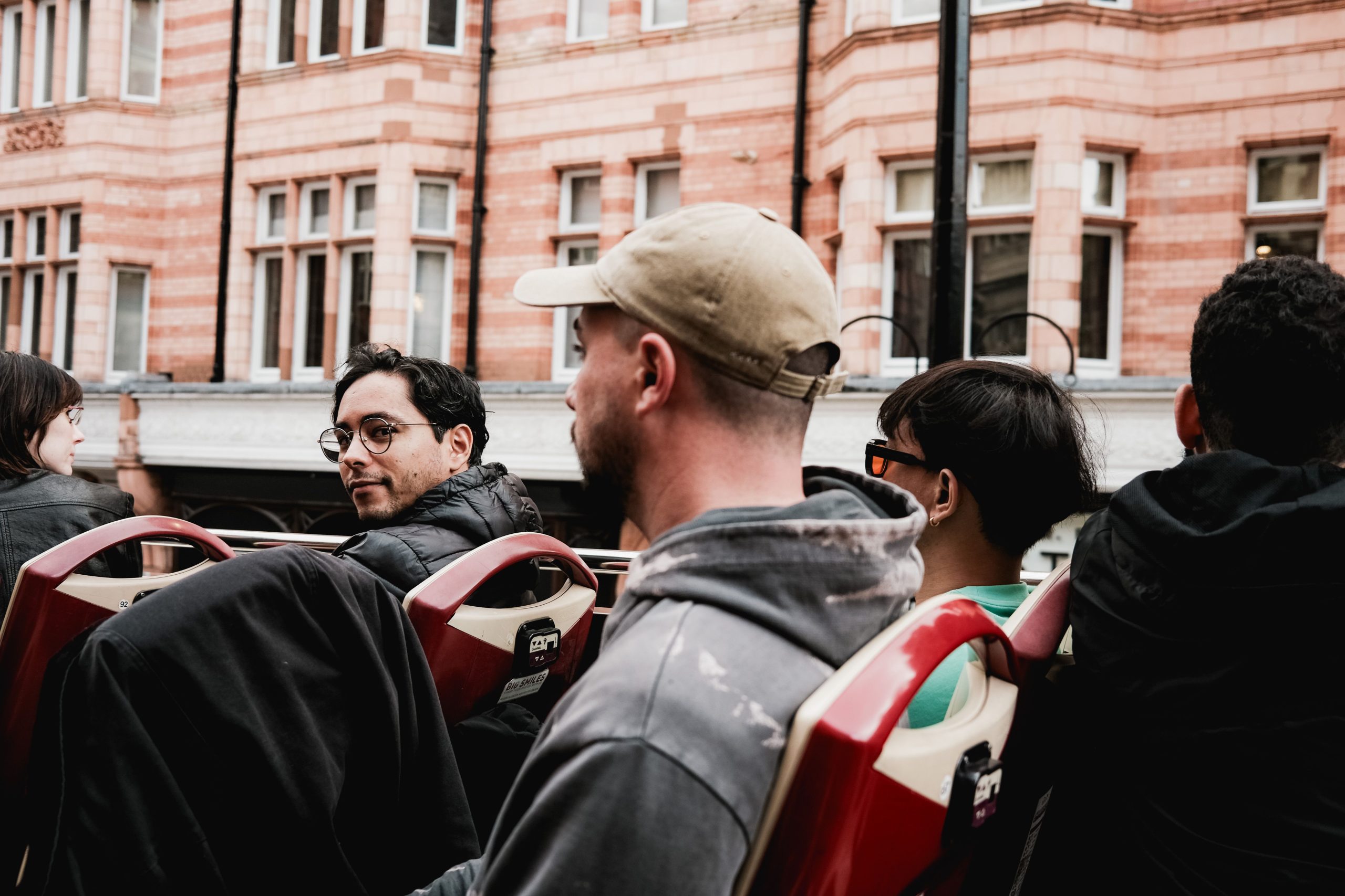 A group of tourists on an open-top bus tour in a vibrant urban setting. Captured in natural light.