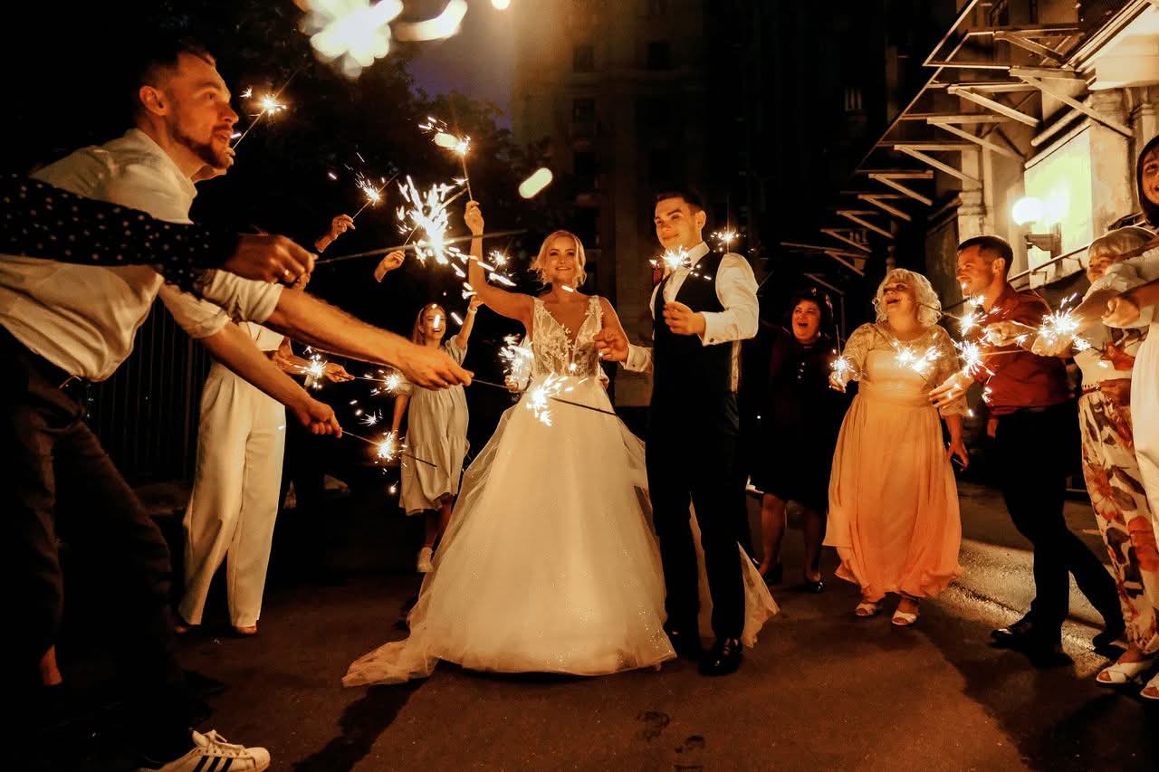 Wedding Transportation NYC for Groups: The Honest 2026 Guide 2 Full body of joyful young bride and groom with sparklers in hands walking near happy guests during wedding celebration in evening